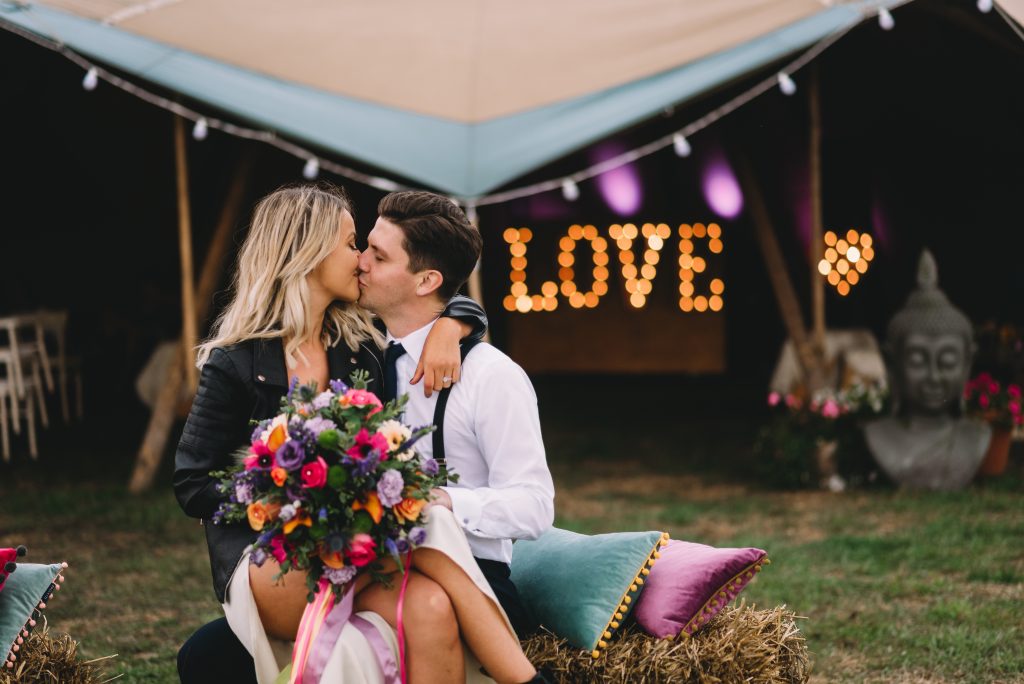 Newly married couple sat on a haystack having a kiss. She is in leather jacket and boots. Link to festival weddings held The Reid Rooms. Newly married couple sat on a haystack having a kiss. She is in leather jacket and boots. Link to festival weddings held The Reid Rooms.