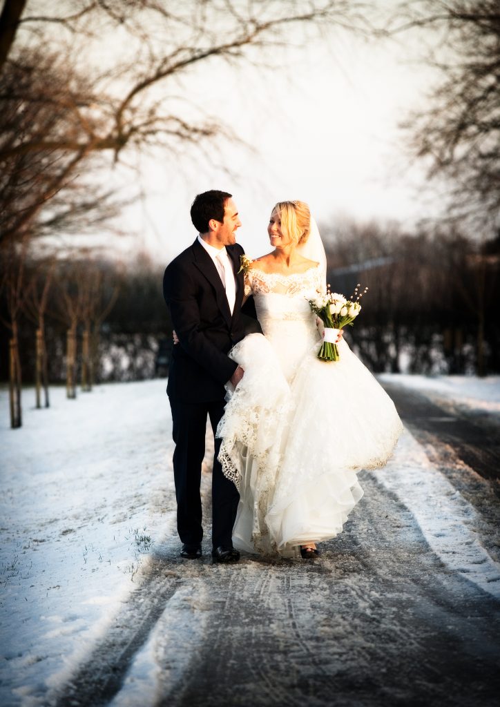 A bride and groom walk down a snowy driveway in the winter at The Reid Rooms. A bride and groom walk down a snowy driveway in the winter at The Reid Rooms.