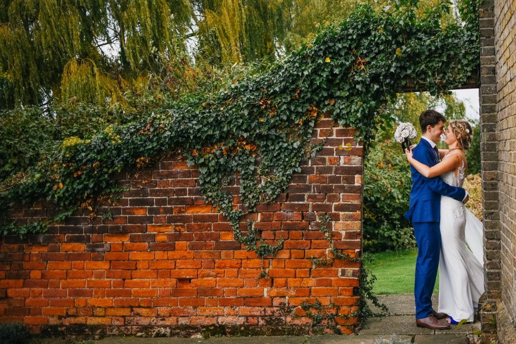 A newly married couple pose in a doorway in a rustic red brick wall covered in trailing green plants. A newly married couple pose in a doorway in a rustic red brick wall covered in trailing green plants.