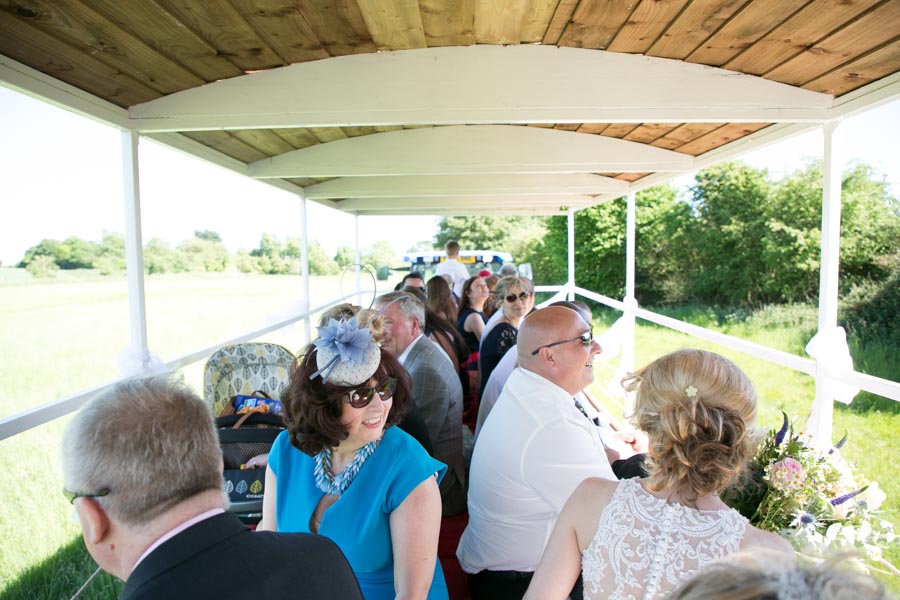 Wedding guests sitting and laughing on a trailer being pulled by a tractor on the way to a wedding ceremony at The Reid Rooms. Wedding guests sitting and laughing on a trailer being pulled by a tractor on the way to a wedding ceremony at The Reid Rooms.