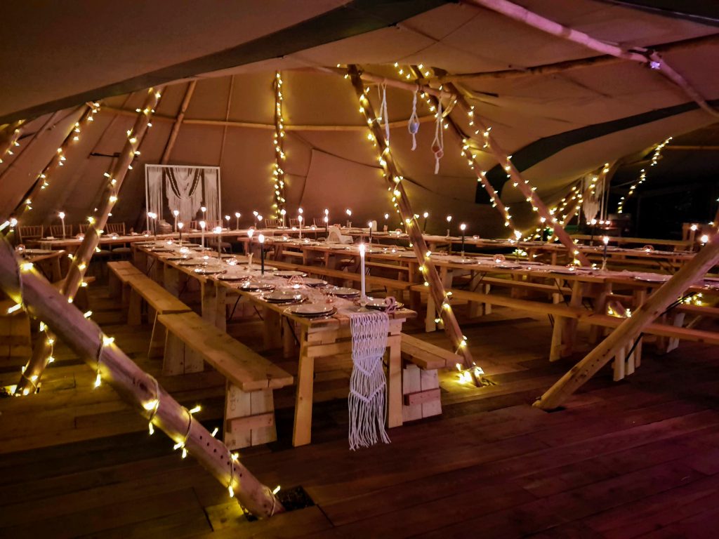 Interior shot of a wedding tipi at The Reid Rooms, covered in fairy lights ready for an evening celebration. Tables are laid out with candles and macramé decorative details. Interior shot of a wedding tipi at The Reid Rooms, covered in fairy lights ready for an evening celebration. Tables are laid out with candles and macramé decorative details.