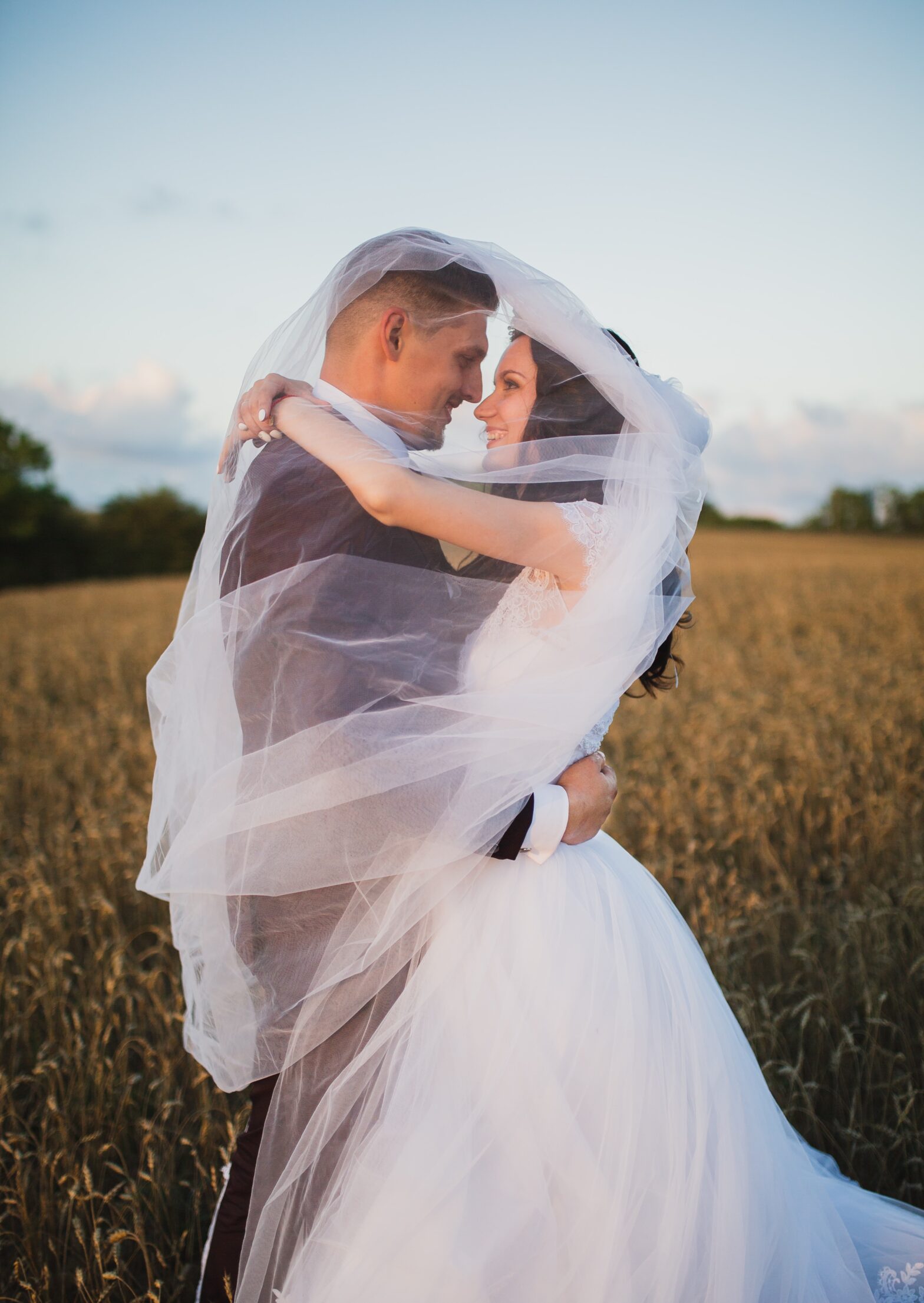 Newly married couple embrace underneath the bride’s veil. They are standing in a field of corn and are alone in their romantic moment together. The image is featured in a blog post about the re-opening of The Reid Rooms wedding venue under the advice of the official government Covid-19 guidelines.