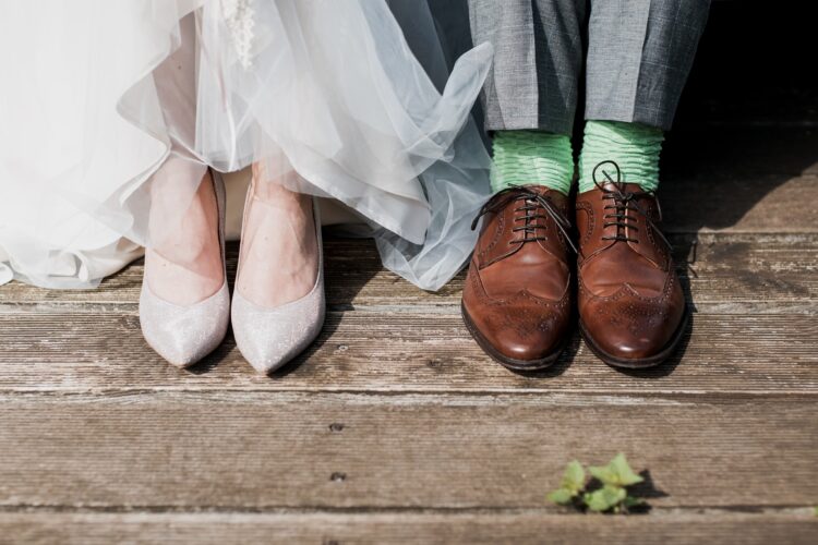 A close up image of the feet of a newly married couple: She is wearing sparkly shoes and he is wearing smart brown brogues and green socks. The image is featured in a blog post about understanding the official government guidance on hosting a wedding and celebration under the Covid-19 guidelines.
