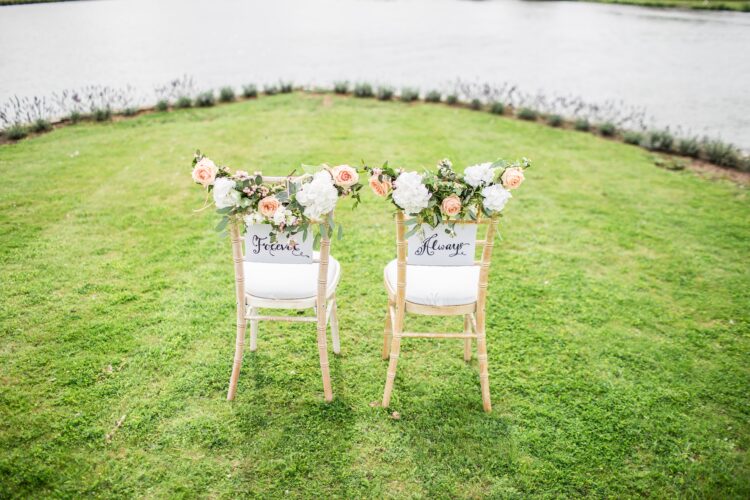 Two chairs decorated with wedding flowers and with signs attached to them saying ‘forever together’ are positioned on their own in the centre of a distanced circle of other chairs. The image is featured in a blog post about understanding the official government guidance on hosting a small wedding and celebration under the Covid- 19 guidelines.